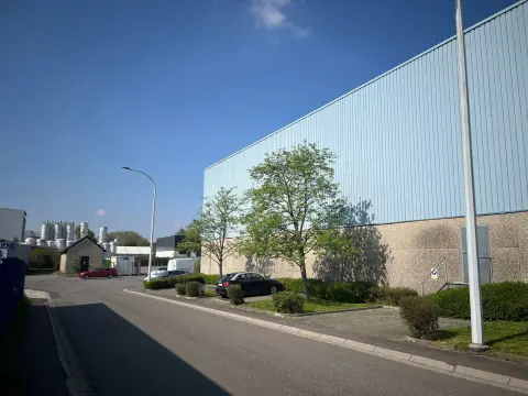 Modernes Industriegebäude mit Wellblechfassade, Parkplatz und Grünflächen unter blauem Himmel.